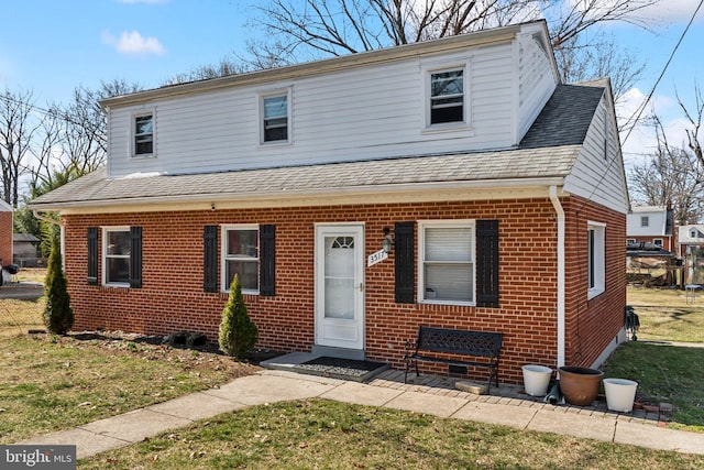 view of front of property with brick siding, a front yard, and roof with shingles