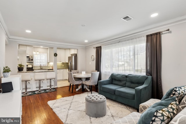 living room featuring visible vents, recessed lighting, crown molding, and wood finished floors