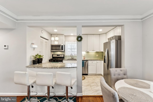 kitchen featuring tasteful backsplash, light stone counters, stainless steel appliances, white cabinetry, and a sink