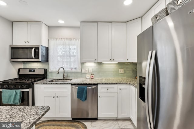 kitchen with a sink, light stone counters, appliances with stainless steel finishes, and white cabinets