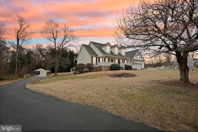 new england style home with a porch, an attached garage, a front yard, and fence