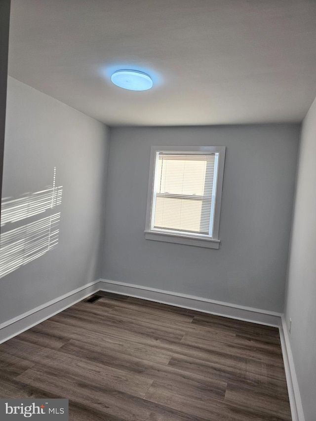 spare room with baseboards and dark wood-style flooring