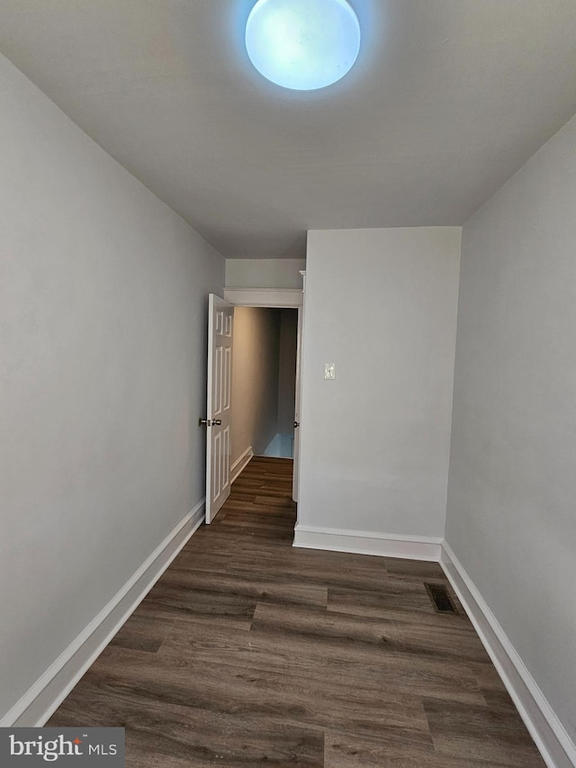 empty room featuring dark wood-type flooring, visible vents, and baseboards