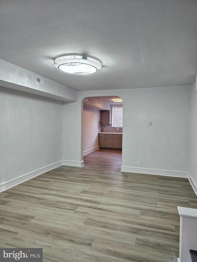 unfurnished living room featuring visible vents, arched walkways, baseboards, and wood finished floors