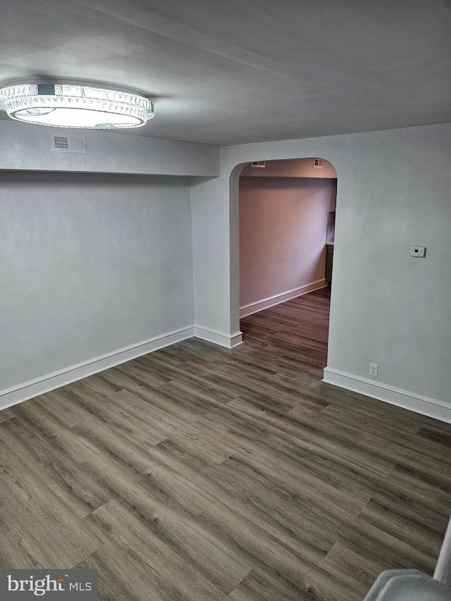 empty room featuring arched walkways, visible vents, baseboards, and wood finished floors