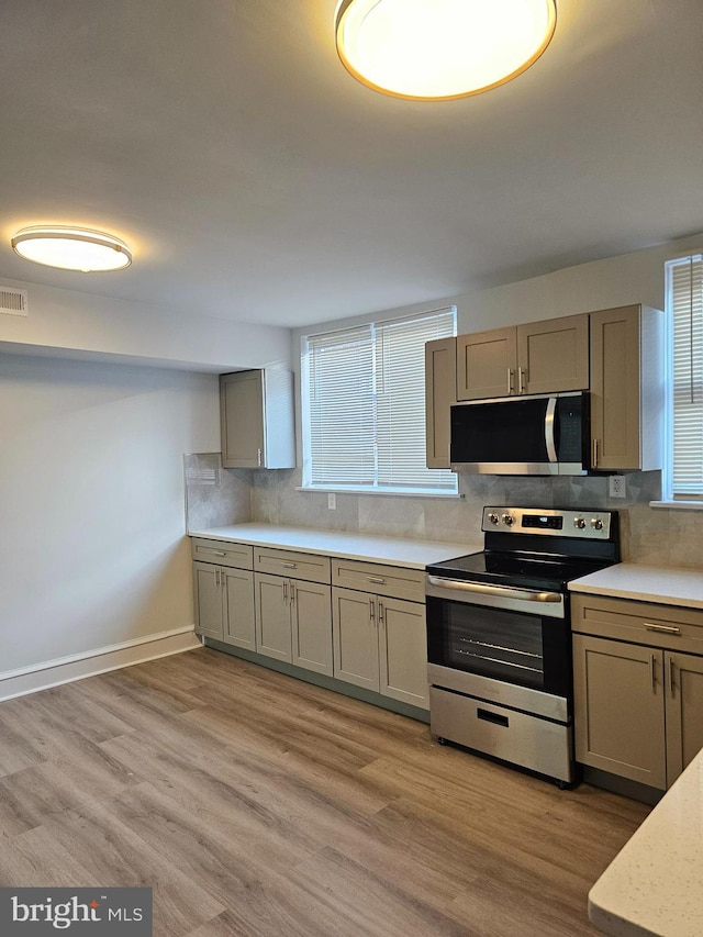 kitchen featuring decorative backsplash, light wood-style flooring, stainless steel appliances, and light countertops