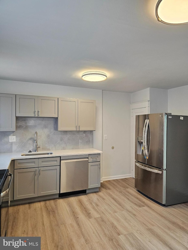 kitchen featuring a sink, appliances with stainless steel finishes, gray cabinetry, and light wood finished floors