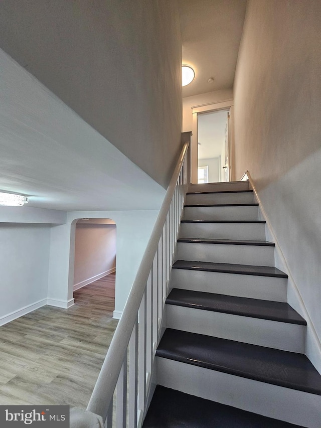 staircase with arched walkways, baseboards, and wood finished floors