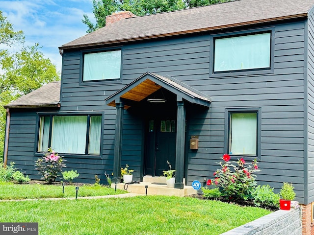 view of front of property featuring roof with shingles, a chimney, and a front yard