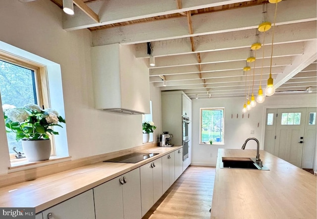 kitchen featuring light countertops, beam ceiling, wall chimney exhaust hood, black electric cooktop, and a sink