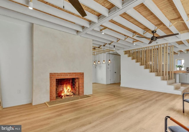 unfurnished living room featuring beamed ceiling, wood finished floors, stairway, a fireplace, and baseboards