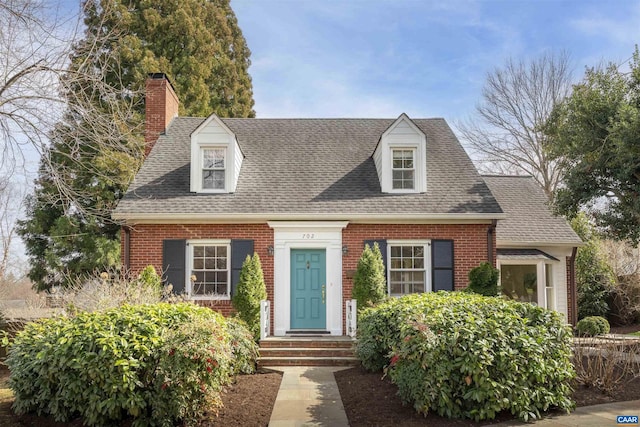 cape cod-style house featuring brick siding, a chimney, and a shingled roof