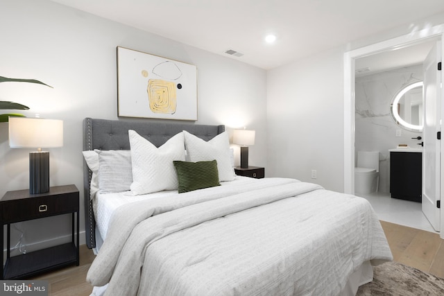 bedroom featuring visible vents, ensuite bath, and light wood-style flooring