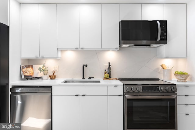 kitchen featuring appliances with stainless steel finishes, white cabinetry, light countertops, and a sink