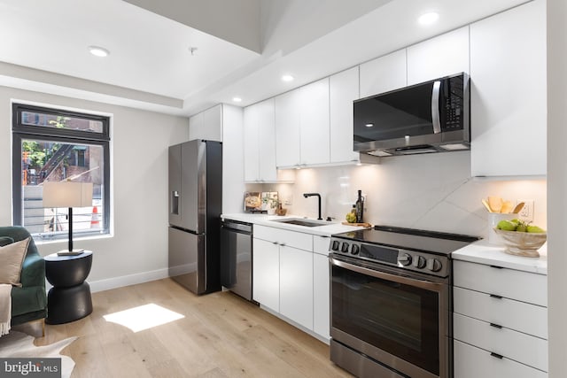 kitchen with light wood finished floors, a sink, stainless steel appliances, white cabinets, and light countertops