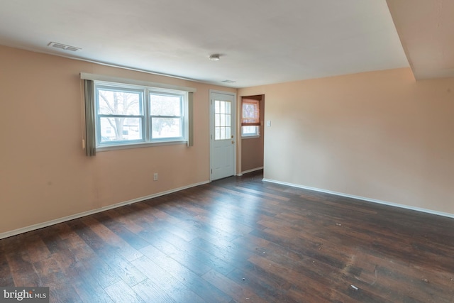 empty room with dark wood-style floors, visible vents, and baseboards