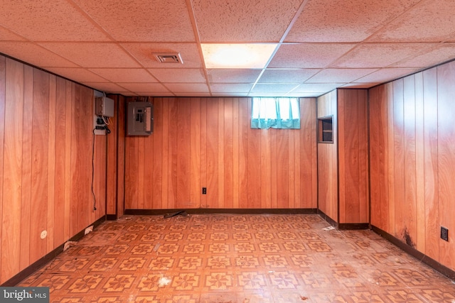 below grade area with electric panel, a drop ceiling, light floors, and wood walls