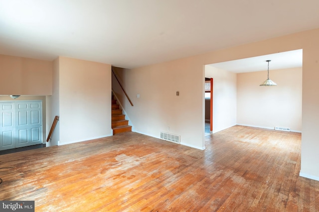 unfurnished living room with visible vents, wood-type flooring, baseboards, and stairs