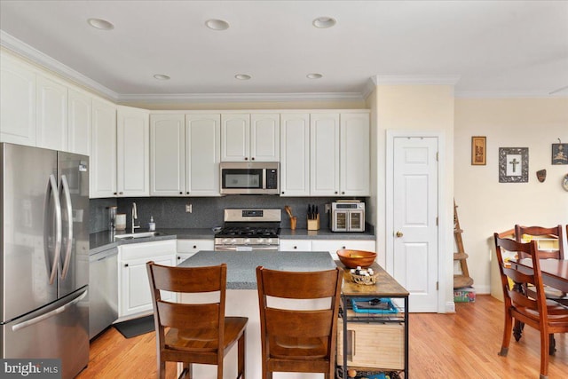 kitchen featuring light wood finished floors, ornamental molding, appliances with stainless steel finishes, and a sink