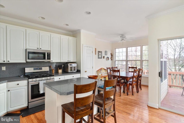 kitchen with stainless steel appliances, dark countertops, light wood-style flooring, and crown molding