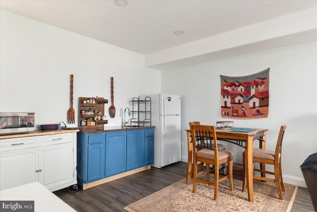 kitchen with baseboards, blue cabinetry, dark wood-style flooring, freestanding refrigerator, and stainless steel microwave