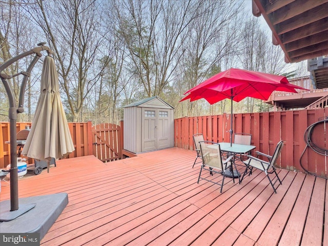 wooden terrace with a fenced backyard, outdoor dining area, a storage shed, and an outdoor structure