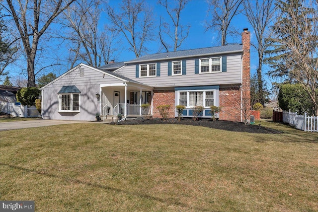 colonial inspired home with brick siding, fence, a front yard, covered porch, and a chimney