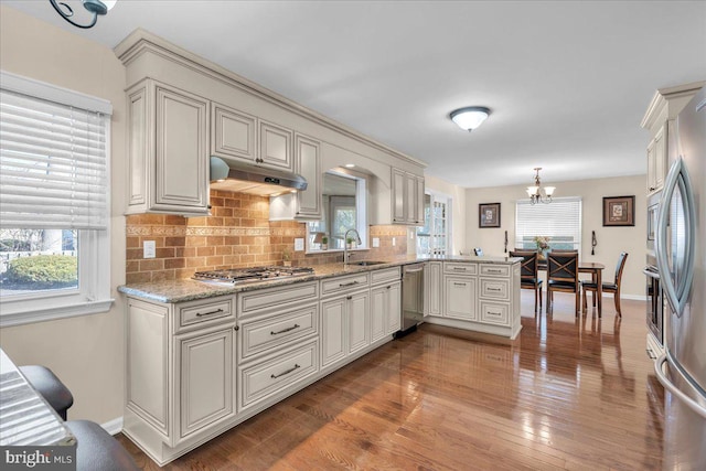 kitchen featuring wood finished floors, a sink, appliances with stainless steel finishes, under cabinet range hood, and backsplash