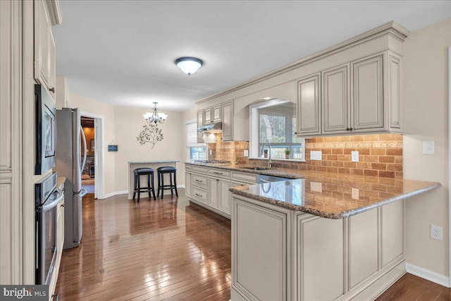 kitchen featuring backsplash, dark wood finished floors, light stone counters, a peninsula, and stainless steel appliances