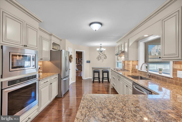 kitchen featuring a sink, light stone countertops, decorative backsplash, appliances with stainless steel finishes, and dark wood-style flooring