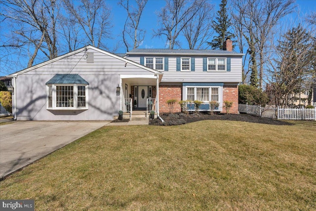 colonial home with fence, a chimney, a front lawn, concrete driveway, and brick siding