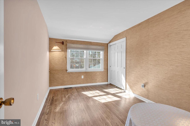 bedroom featuring wood finished floors, visible vents, baseboards, lofted ceiling, and a closet