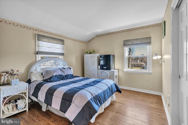 bedroom with a closet, wood finished floors, baseboards, and vaulted ceiling