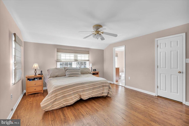 bedroom with ensuite bath, lofted ceiling, wood finished floors, and baseboards