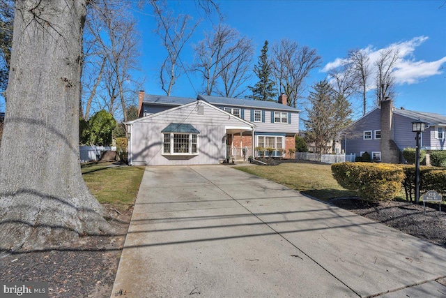 view of front facade with fence, concrete driveway, a front yard, covered porch, and a chimney