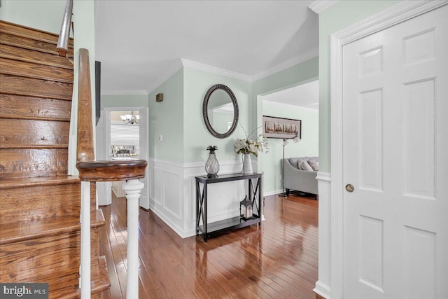 corridor with hardwood / wood-style floors, stairs, wainscoting, crown molding, and a chandelier