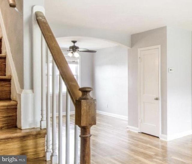 staircase featuring ceiling fan, baseboards, arched walkways, and wood finished floors