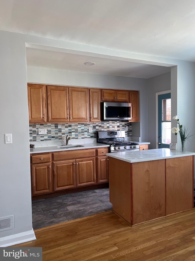 kitchen featuring visible vents, a sink, dark wood finished floors, stainless steel appliances, and brown cabinetry