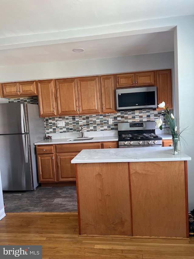 kitchen with brown cabinetry, light countertops, dark wood-style floors, stainless steel appliances, and a sink