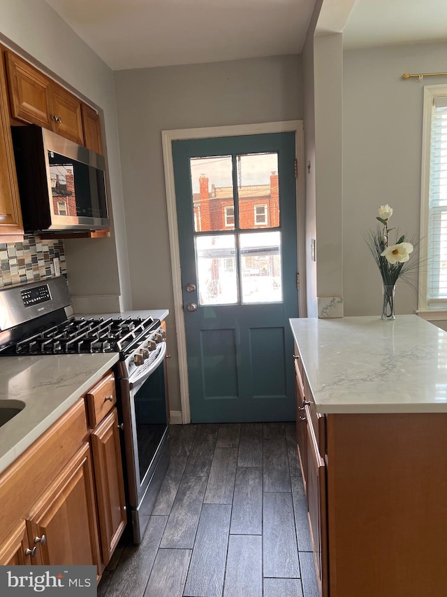 kitchen with dark wood-type flooring, light stone counters, decorative backsplash, brown cabinetry, and stainless steel appliances