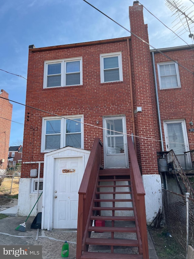 back of property with brick siding, a chimney, and fence