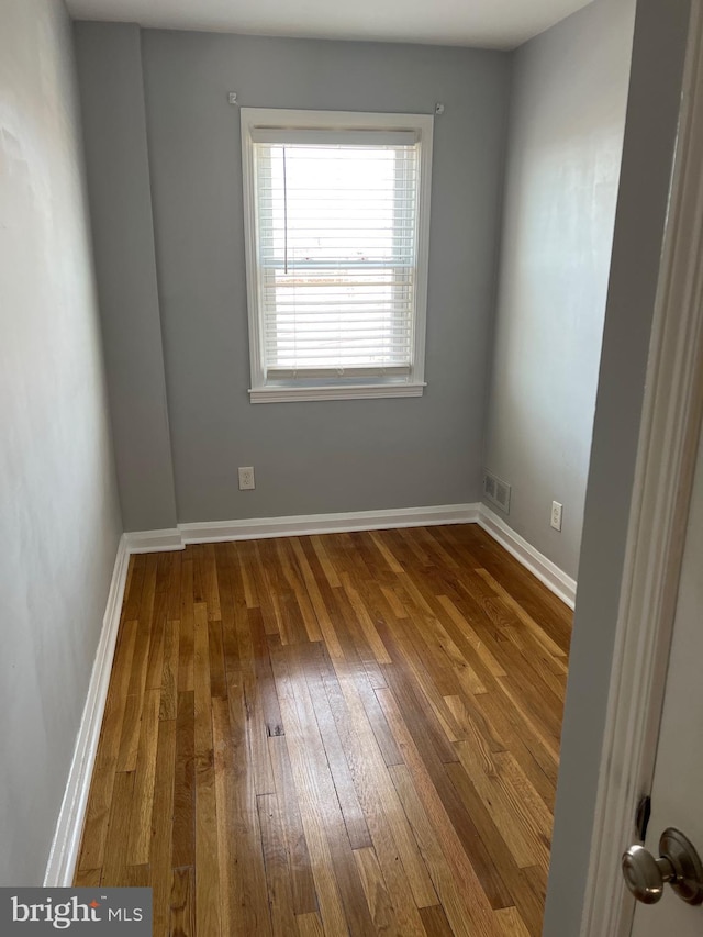 unfurnished room featuring hardwood / wood-style floors, visible vents, and baseboards