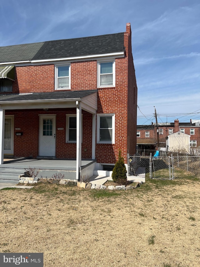 rear view of house featuring a yard, brick siding, covered porch, and a gate