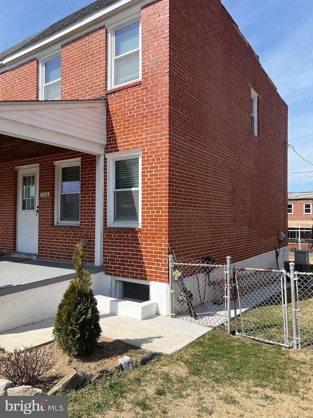 view of side of property featuring a gate, fence, brick siding, and a lawn