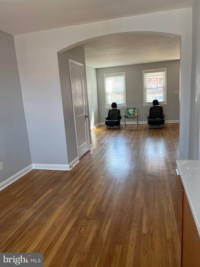 interior space with baseboards, arched walkways, and dark wood-style flooring