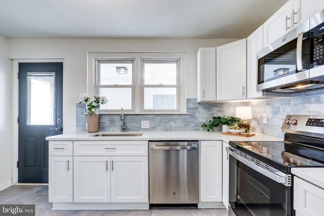 kitchen featuring light countertops, decorative backsplash, white cabinets, stainless steel appliances, and a sink