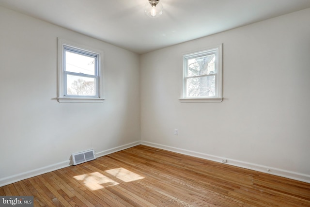 spare room featuring light wood-style floors, a healthy amount of sunlight, and visible vents