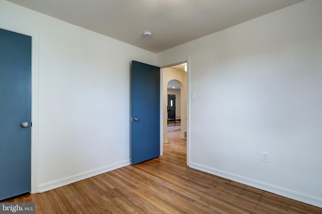 unfurnished room featuring baseboards, arched walkways, and hardwood / wood-style floors