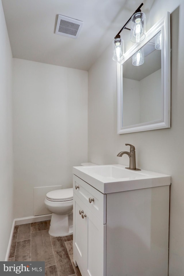 half bathroom with wood finish floors, visible vents, toilet, baseboards, and vanity