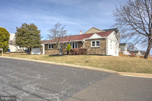 ranch-style home with an attached garage, a shingled roof, a chimney, a front lawn, and stone siding